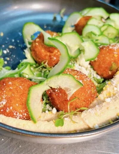 Close-up: Golden falafel on hummus, garnished with cucumber, microgreens, and feta.