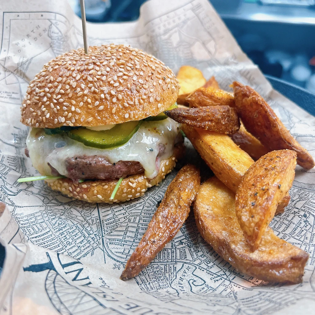 Cheeseburger with melted white cheese, pickles, arugula, and seasoned potato wedges.