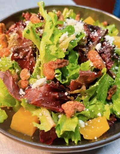 A fresh salad with mixed greens, feta, golden nuts, and yellow cubes.