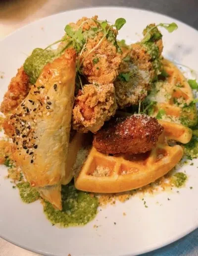 Crispy fried chicken, waffle, and pastry with green sauce and microgreens.