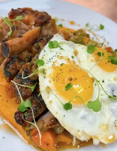 Grilled pork chops, two sunny-side eggs, vegetables, and sauce.