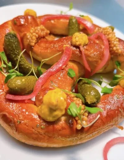 Savory gourmet pretzel garnished with gherkins, two mustards, red onions, microgreens.