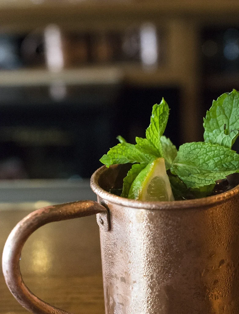 Close-up of a frosty copper mug cocktail garnished with mint and lime.