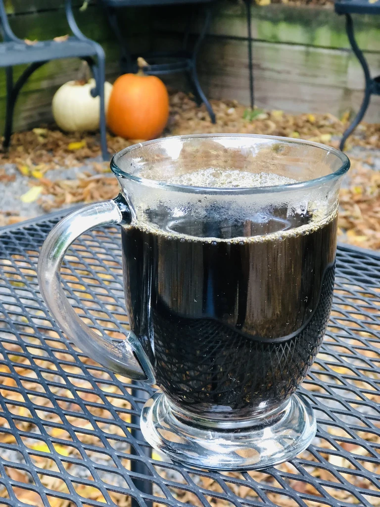 Clear glass mug of coffee on black mesh table, autumn pumpkins.