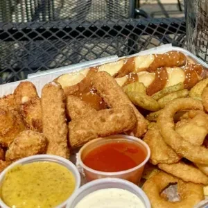 Platter of fried pretzel bites, mozzarella sticks, onion rings, and dipping sauces.