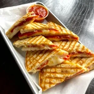 Grilled sandwiches with cheese and red filling, grill marks, and dipping sauce.