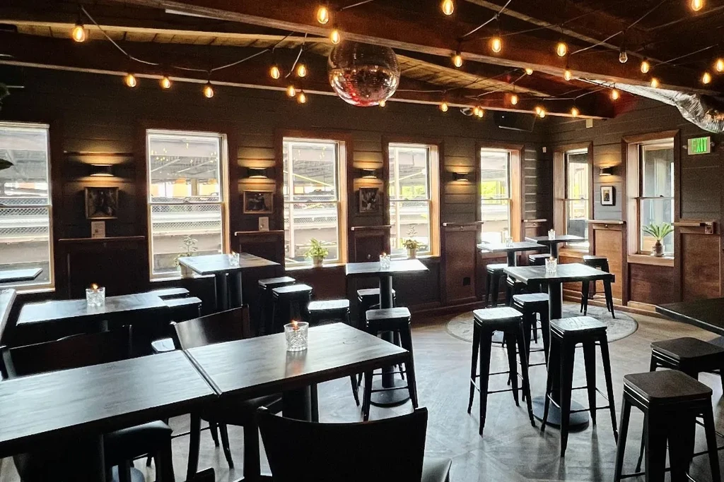 Dimly lit restaurant interior with disco ball, Edison lights, and dark furniture.