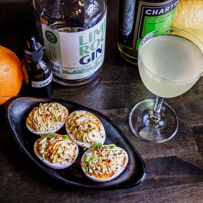 A still life of deviled eggs, a cocktail, gin, and Chartreuse bottles.
