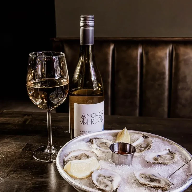 Bottle of white wine, glass, and oysters on ice.