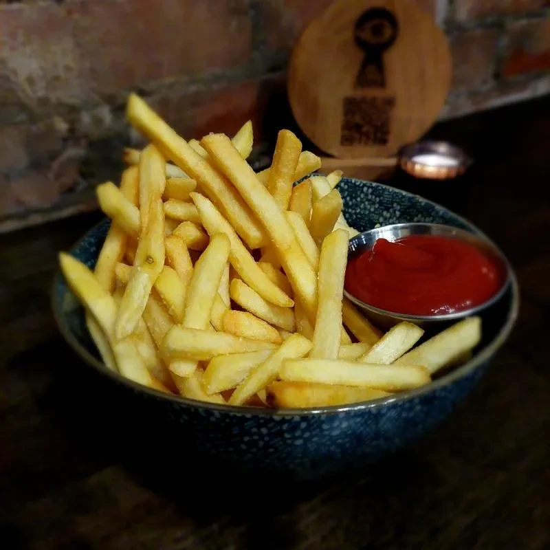 Crispy golden french fries in a dark blue bowl with ketchup.