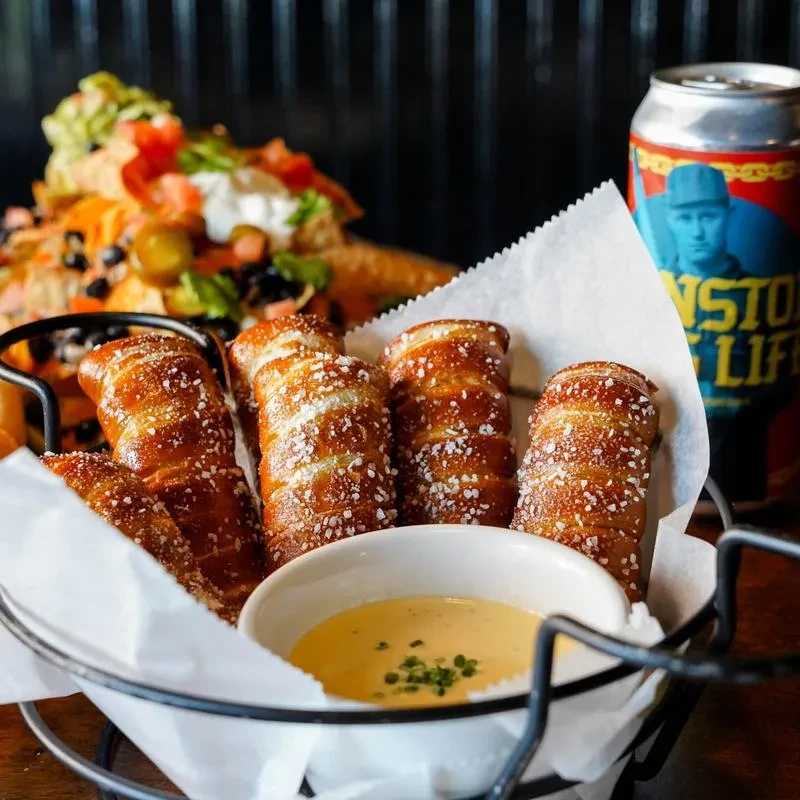 Golden pretzel bites, cheese dip, nachos, and a branded beverage on a table.