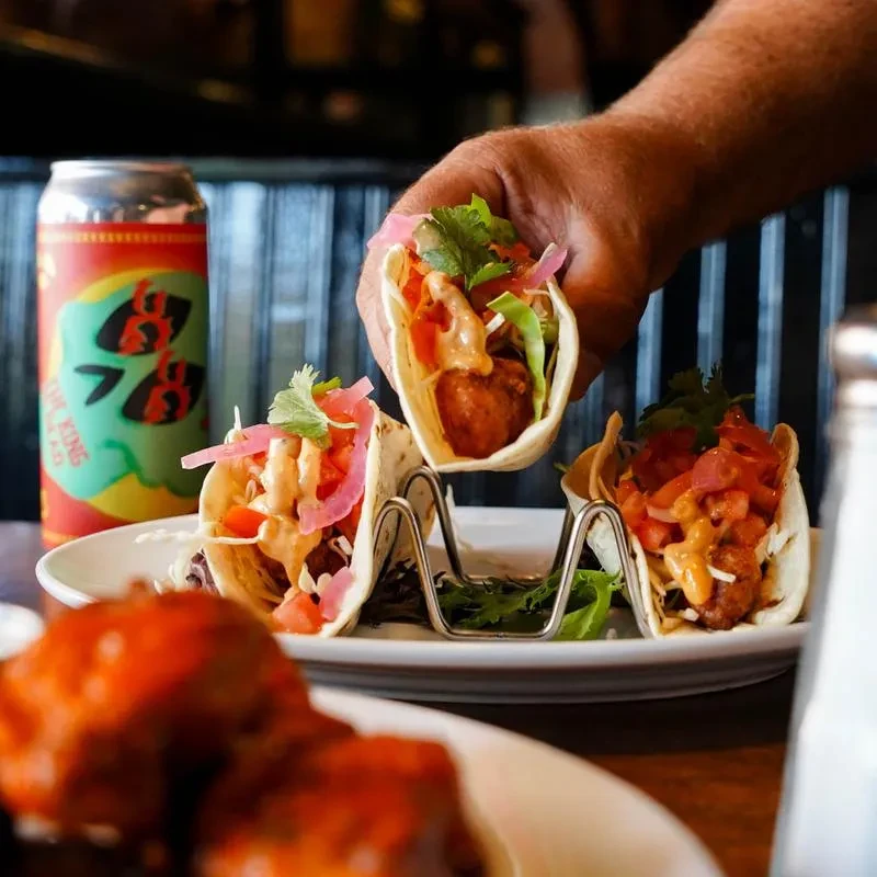 Hand holding one of several fried chicken tacos with toppings.