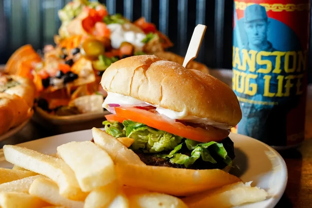 Hamburger and fries on a plate, with nachos and a drink can.