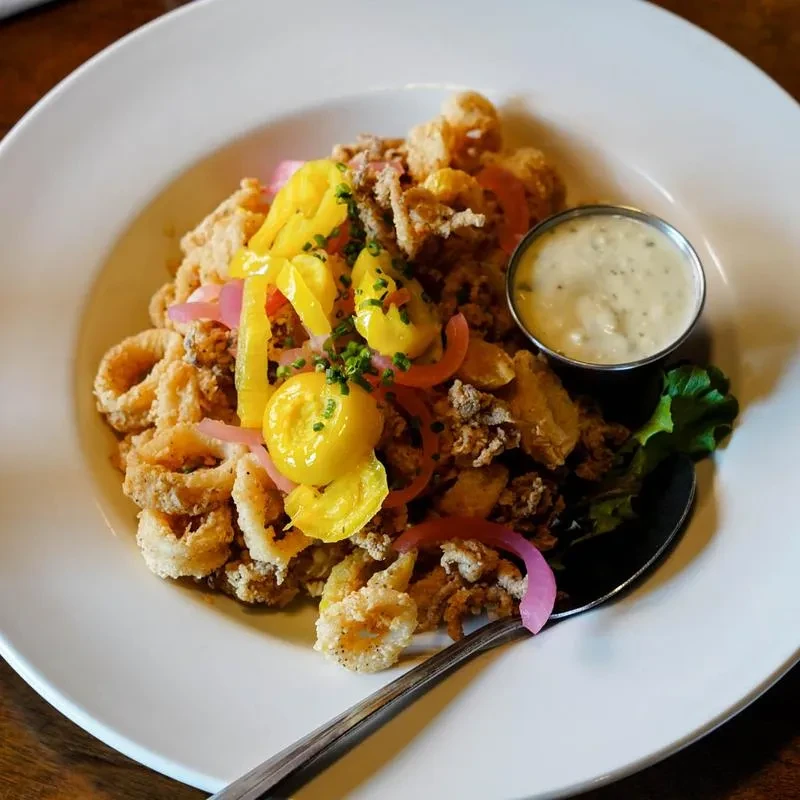 Close-up: Fried calamari topped with pickled peppers, onions, herbs, sauce.