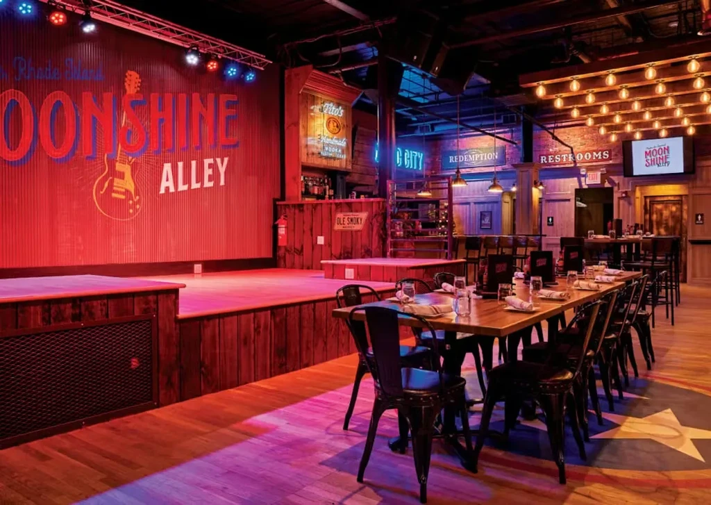 Empty, rustic-industrial bar interior with 'Rhode Island Moonshine Alley' stage.