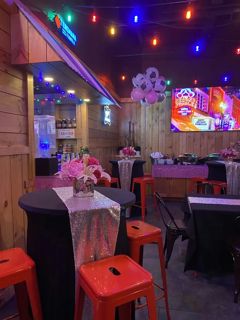 Festive bar with sequined tables, flower centerpieces, colorful lights, birthday sign.