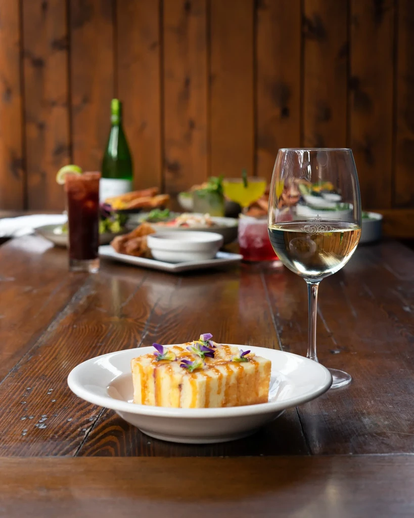 Dessert with caramel, purple flowers, and wine on a rustic table.