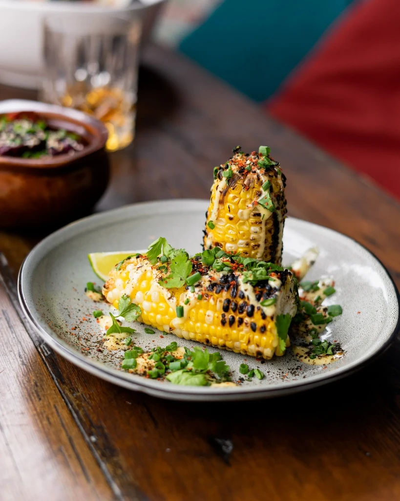 Grilled corn halves with creamy sauce, herbs, and spices on a rustic table.
