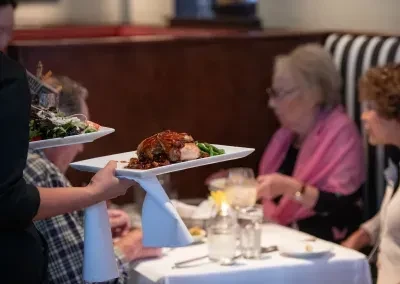 Server carries two plated dishes: a main course and a fresh salad.