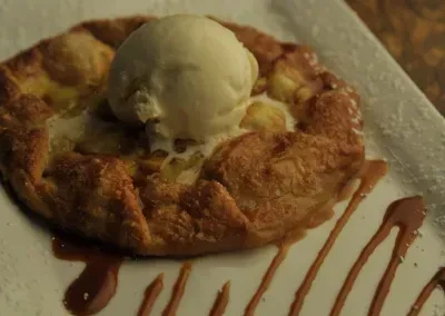 Close-up of golden fruit tart with melting vanilla ice cream and sauce.