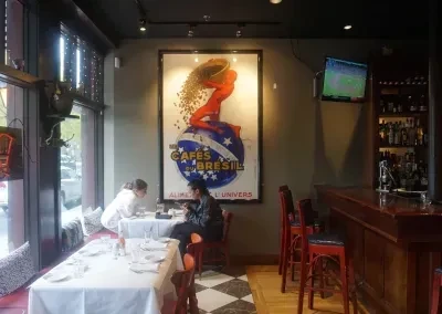 Restaurant interior with dining area, bar, and vintage 'Cafes du Bresil' poster.