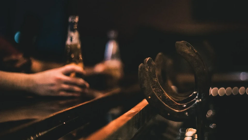 Rustic horseshoe and hand near beer bottle on a dim bar.
