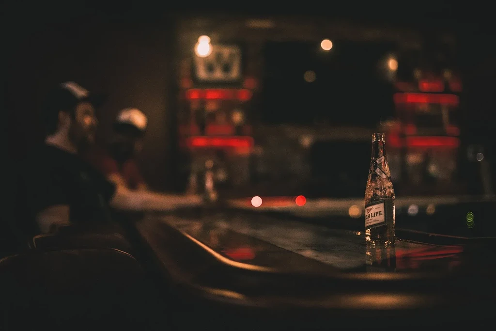 Empty Miller High Life bottle with condensation on a dimly lit bar counter.