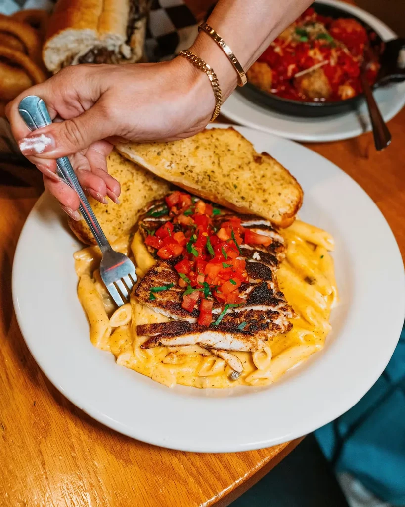 Hand forks blackened chicken on penne pasta with garlic bread.