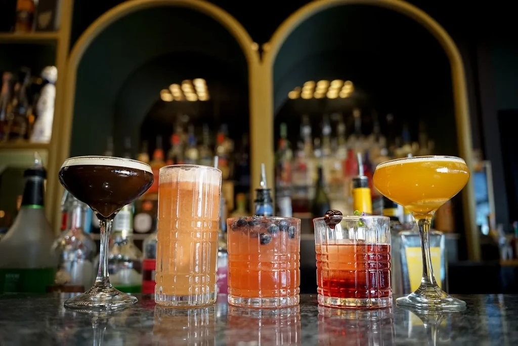 Five distinct cocktails in varied glasses on a bar counter.