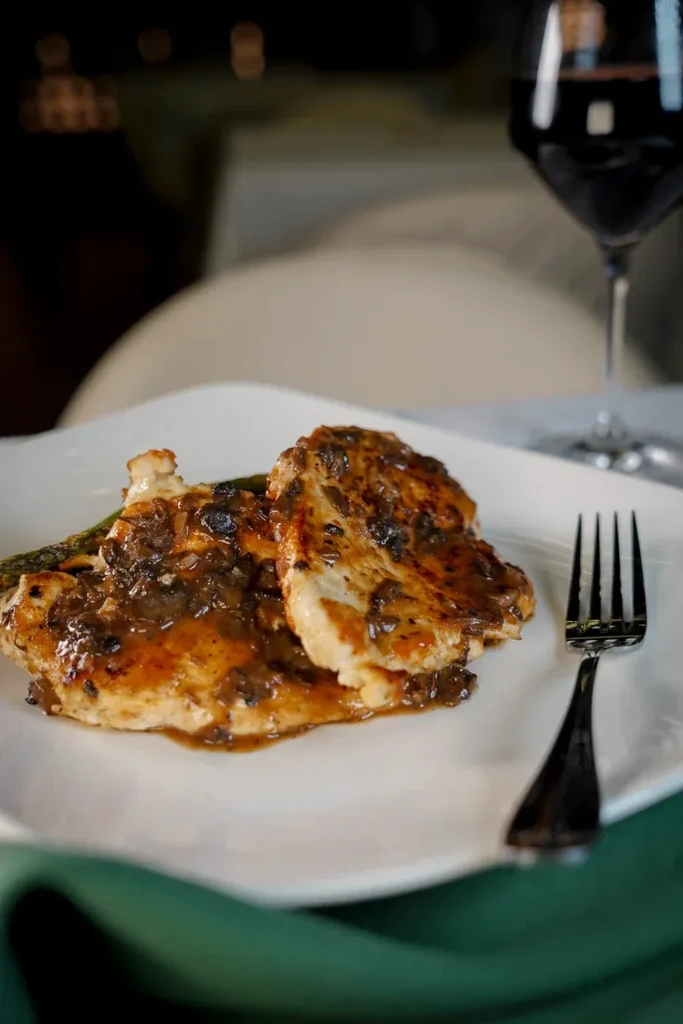 Two chicken breasts with dark sauce on a white plate and fork.