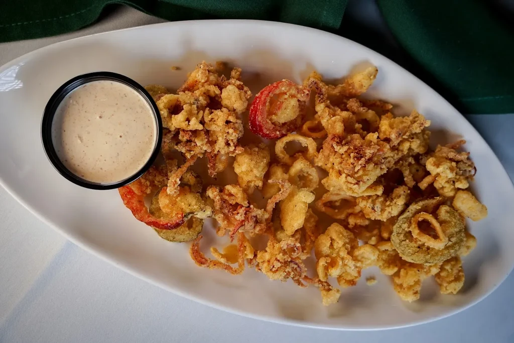 Golden fried calamari and vegetables on a white plate with dipping sauce.