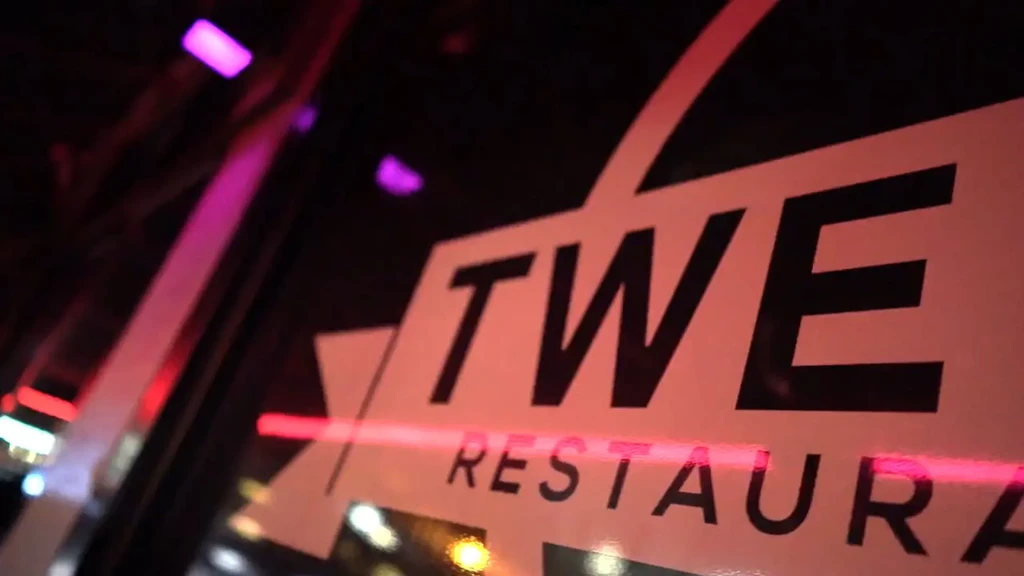 Close-up of TWE RESTAURANT sign glowing with pink and purple neon.