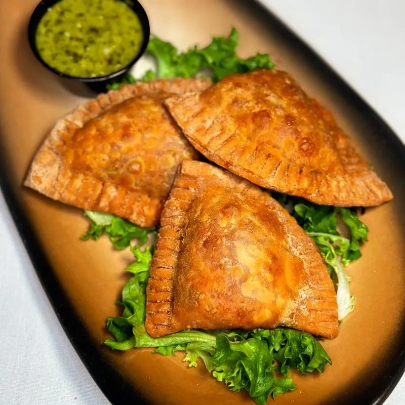 Three golden-brown, filled pastries on lettuce, with green dipping sauce.