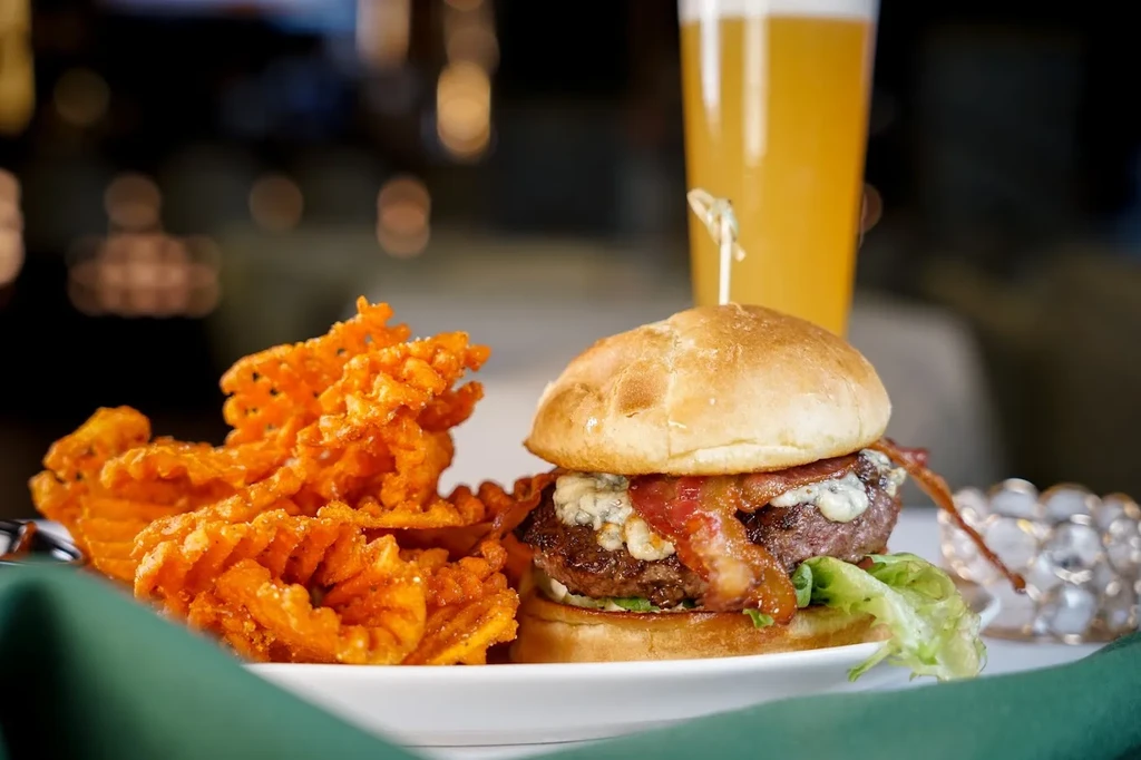 Close-up of blue cheese burger, bacon, waffle fries, and beer.