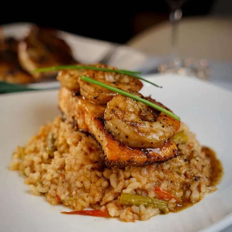 Seared salmon and grilled shrimp over vegetable rice, garnished with chives.