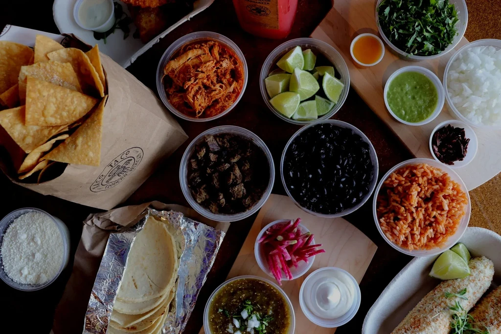 Overhead shot of a colorful Mexican food spread in takeout containers.