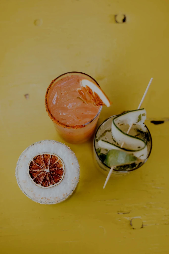 Three colorful garnished drinks on a bright yellow table.
