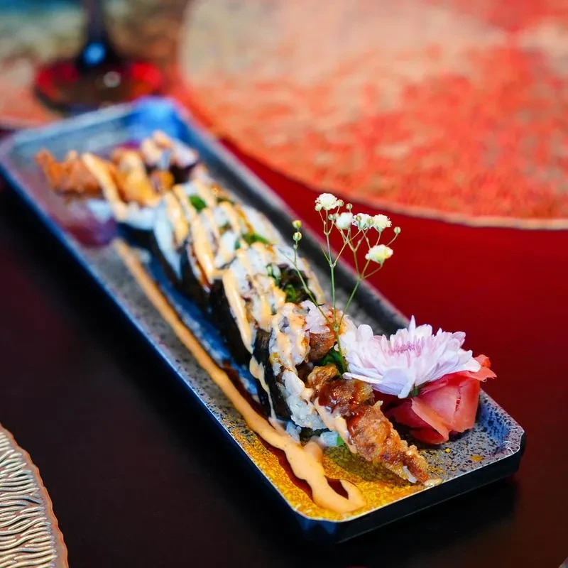 Sushi rolls with tempura, creamy sauce, flowers, and pickled ginger.