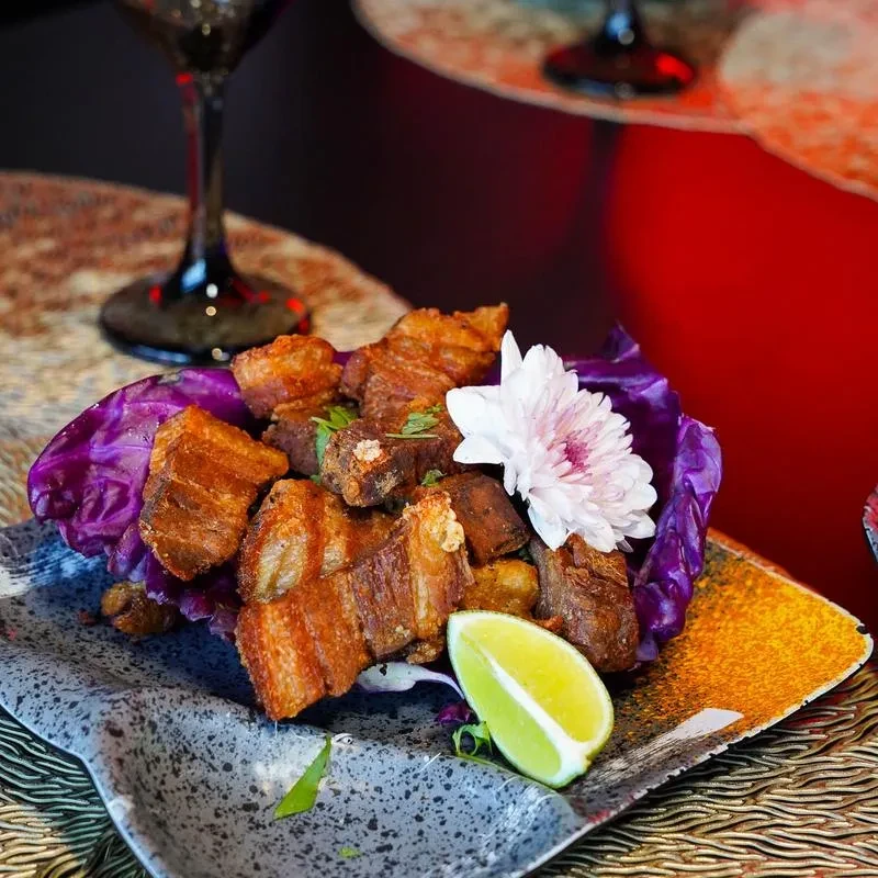 Crispy fried pork belly with purple cabbage, lime, and flower.
