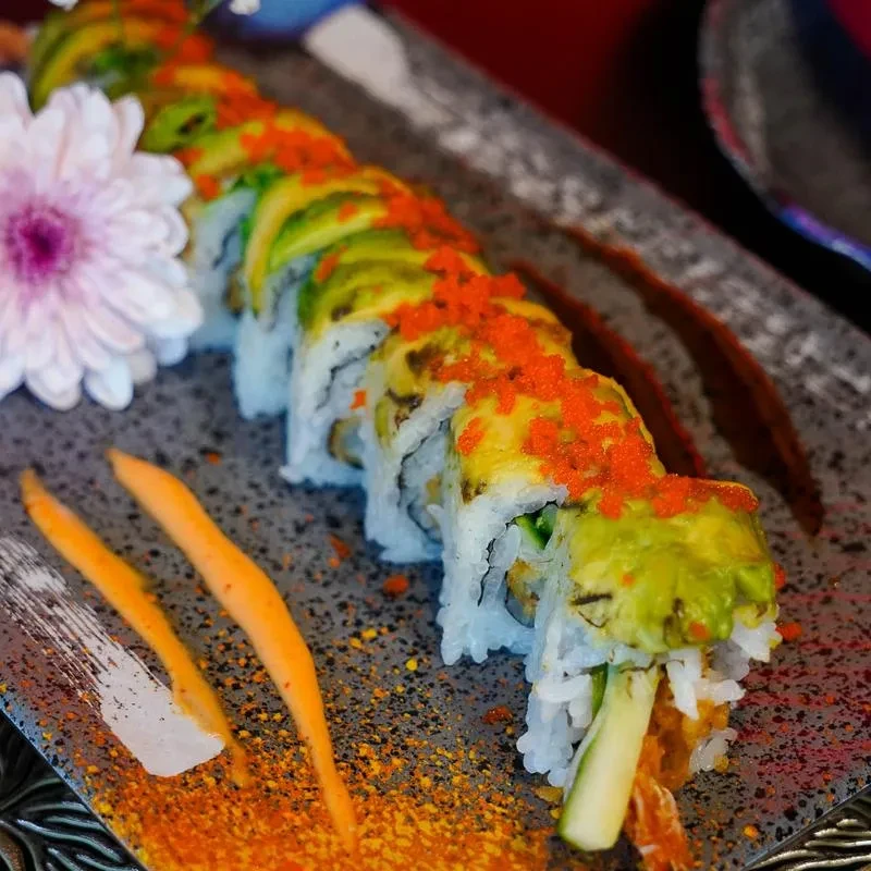Sushi dragon roll topped with avocado, tobiko, sauce, and a decorative flower.