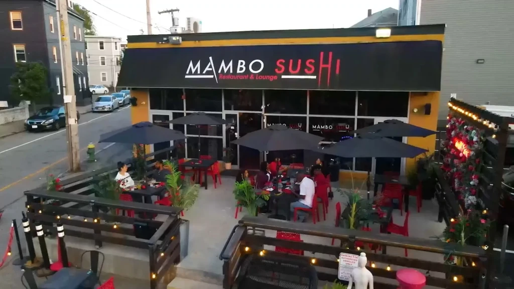 Mambo Sushi restaurant with people dining on its outdoor patio at dusk.