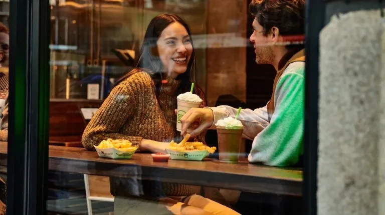 Man and woman converse over fries and milkshakes at a counter.