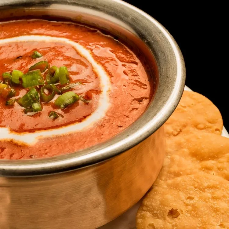 Orange-red curry with cream, green onions, and puffed flatbreads.