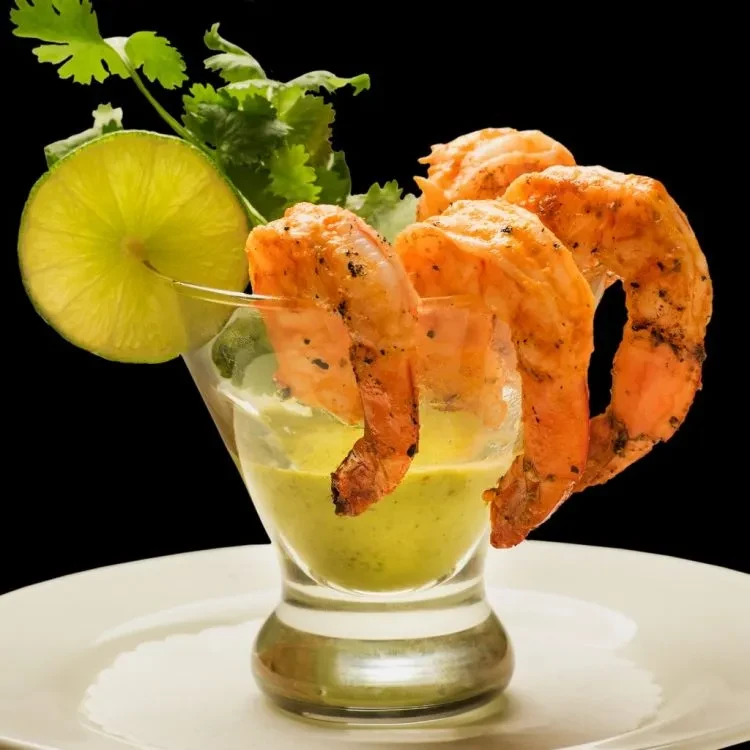 Three shrimp over green sauce in glass, with lime and cilantro.