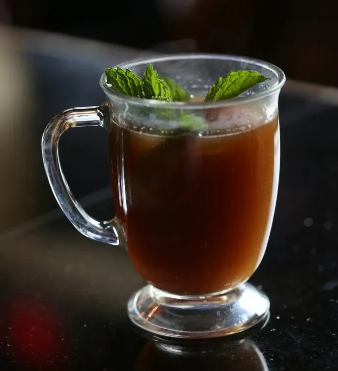 Clear glass mug with dark amber drink and fresh mint leaves.
