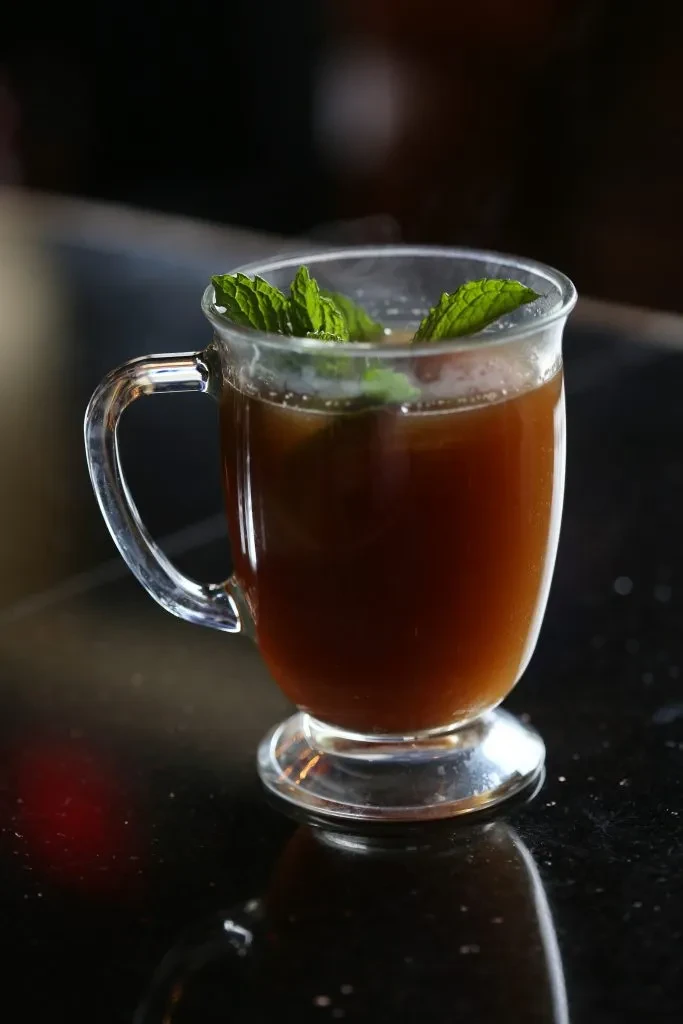 Glass mug with dark amber drink, garnished with fresh mint.