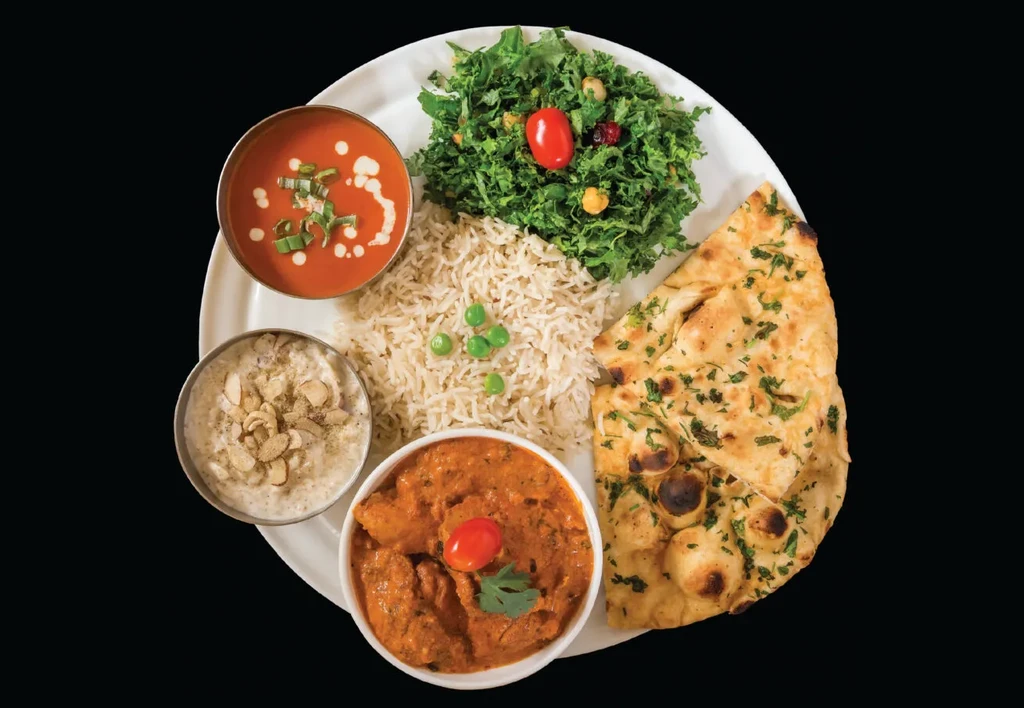 Overhead shot of a colorful thali meal with rice, naan, and curries.