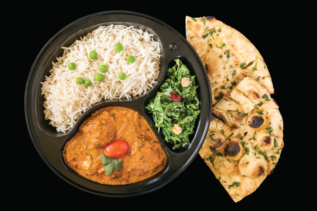 Colorful Indian meal with rice, curry, salad, and naan on black plate.