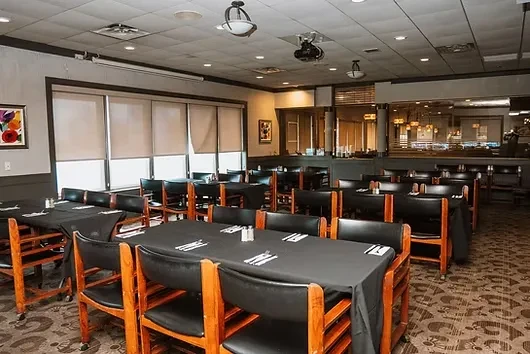 Spacious, empty restaurant dining room with set tables and large windows.