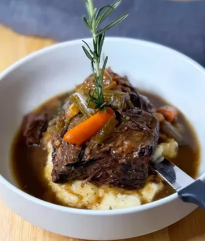 Close-up: Braised meat, mashed potatoes, gravy, vegetables, and rosemary.